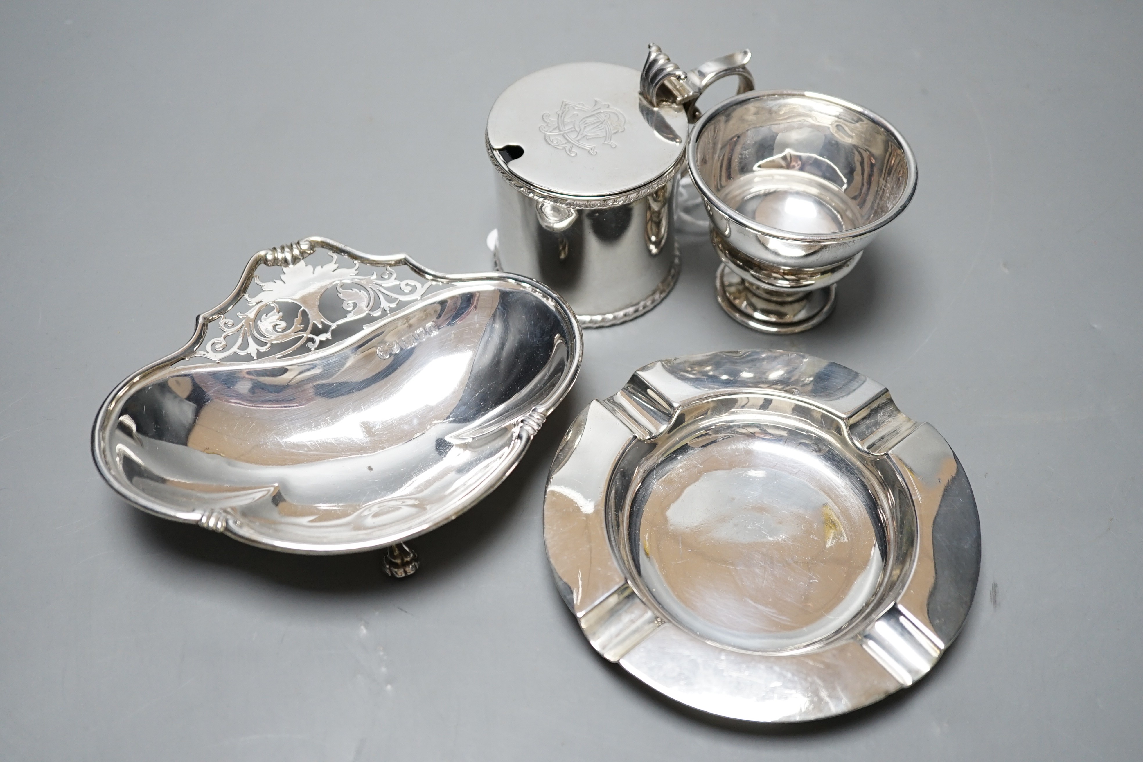 A late Victorian silver mustard pot, Sheffield, 1896, a later silver ashtray and small bowl and an Edwardian pieced silver shaped dish by Elkington & Co, London, 1909.